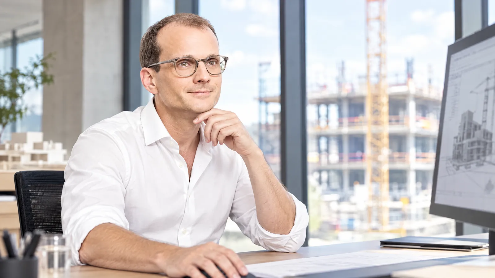 KI-Darstellung des Betreibers am Schreibtisch vor einem Fenster mit Baustellenblick.